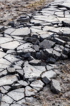 A detailed close up of a significantly cracked and damaged asphalt road surface