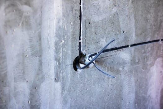 There is a noticeable hole present in a concrete wall, and from this opening, various wires are protruding outward from inside it