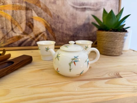 Small porcelain teapot with bamboo motif on wooden table. Harmony, tea culture, and peaceful atmosphere of traditional tea ceremony.
