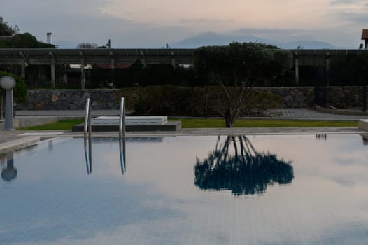 Calm waters of a pool mirror the surrounding trees and structures as evening approaches. Soft hues of dusk create a peaceful ambiance, inviting relaxation.