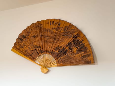 Traditional decorative fan on white wall with detailed historical landscape. Cultural heritage and visual storytelling through Asian artistry