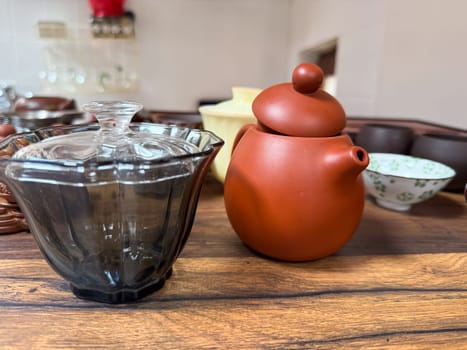Clay teapot and glass bowl on wooden tea table. Traditional tea ceremony tools used for mindful brewing and aesthetic appreciation of tea culture.