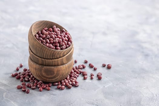 Wooden bowls full of dried red azuki beans on gray table closeup, copy space. Healthy vegetarian food, legumes protein source. Traditional East Asiancousin ingredient
