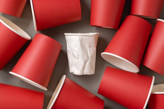 Disposable new red paper cups and crumpled used white one on gray top view. Empty single-use cardboard coffee cups flat lay. Consumerism concept in modern world