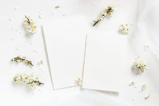 Blank cards near tulle and wild plums white flowers top view, mockup. Pastel vertical cards for spring party design or romantic wedding stationery. Close to nature or mothers day concept