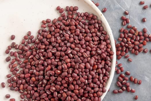 Ceramic plate full of dried red azuki beans on gray table top view. Healthy vegetarian food, legumes protein source. Traditional East Asiancousin ingredient