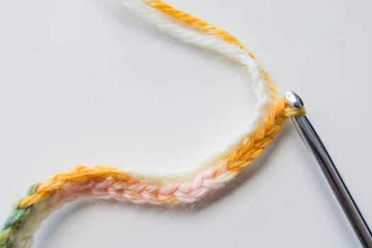 Close up of colorful crochet chain and silver hook on white background.