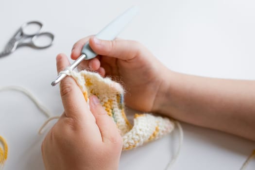 Close up of young caucasian child crocheting with yellow and white yarn.