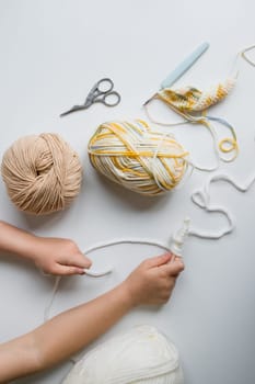 Child crafting with yarn and tools on white surface.