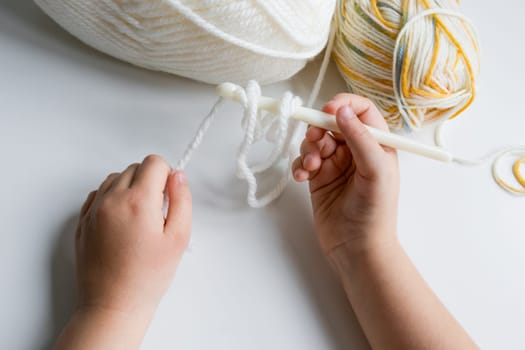 Childs hands crocheting with white and multicolored yarn.