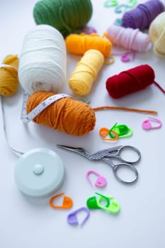 Colorful yarn and knitting supplies with measuring tape and scissors on white background.
