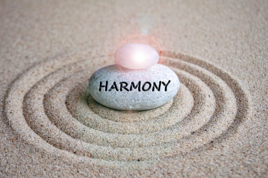 Harmony text engraved on zen stock with shining stone on top of sands.