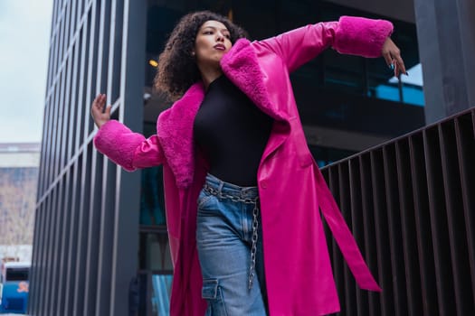 African american dancer with curly hair wearing a pink coat, expressing movement and energy in an urban environment. Modern fashion, contemporary dance,and artistic performance against a city backdrop