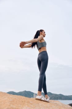 A fit young woman in stylish workout attire stretches by the beach, showcasing confidence and vitality, ideal for themes of fitness, wellness, and healthy lifestyle