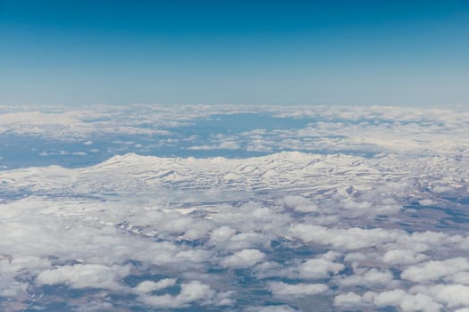 landscape on snowy mountains with clouds from the window of an airplane
