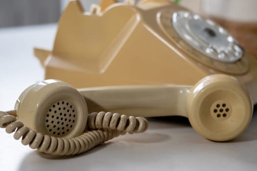 A yellow rotary telephone with a white cord sits on a table. It is old.