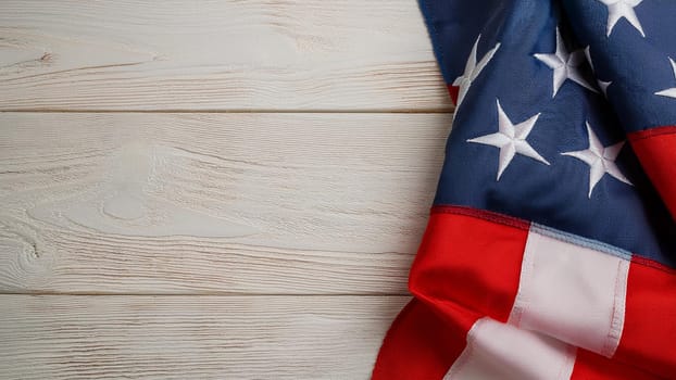 A red, white and blue American flag is on a wooden background. The flag is spread out and the stars are visible. The flag is a symbol of patriotism and pride
