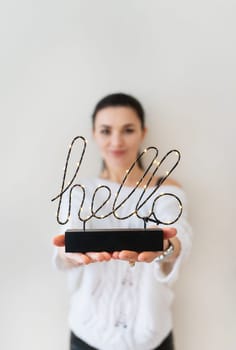 A woman holds a lighted 'hello' sign, offering a warm and welcoming greeting.