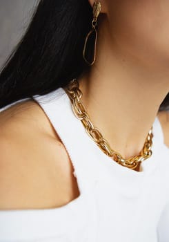Elegant woman with long black hair models gold chain necklace and earrings.