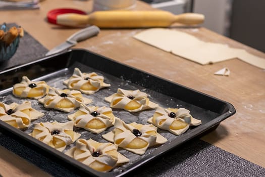 Puff pastry with pineapple wedges wrapped and cherry on top, on the baking tray in the kitchen counter top