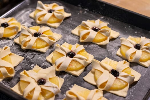 Puff pastry with pineapple wedges wrapped and cherry on top, on the baking tray in the kitchen counter top
