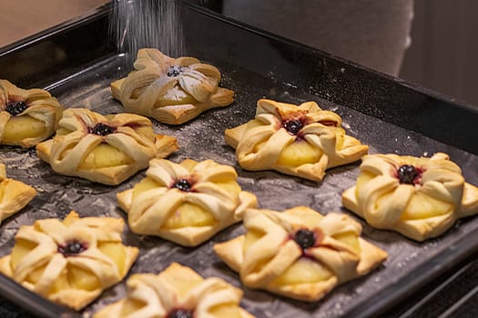 A woman dusts a pineapple wedge and cherry wrapped in a puff pastry with powdered sugar