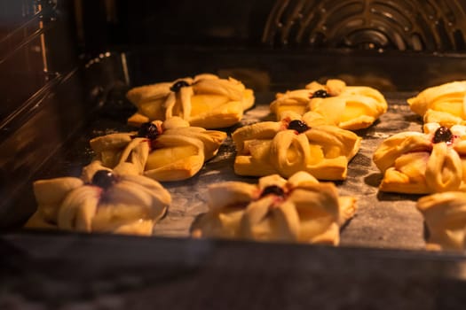 Puff pastry with pineapple wedges wrapped and cherry on top, on the baking tray baking in the oven
