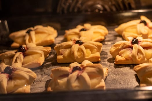 Puff pastry with pineapple wedges wrapped and cherry on top, on the baking tray baking in the oven