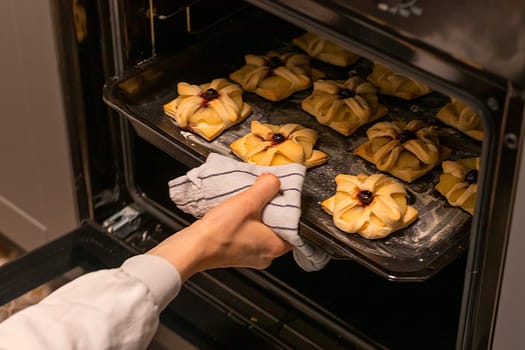 A woman picks baking tray with puff pastry with pineapple wedges wrapped and cherry on top from the oven