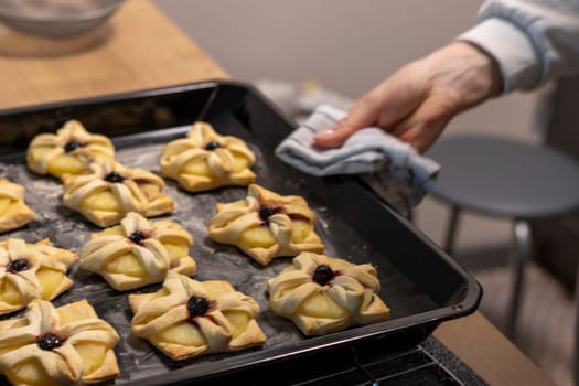 A woman places baking tray with with puff pastry with pineapple wedges wrapped and cherry on top from the oven to the kitchen counter top