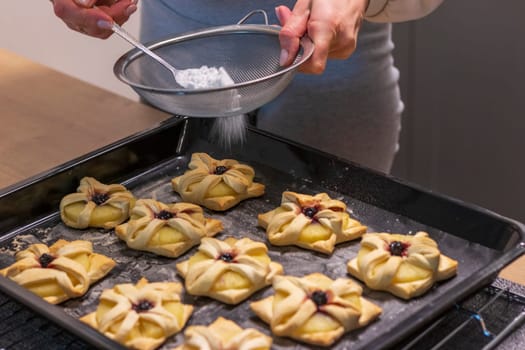 A woman dusts a pineapple wedge and cherry wrapped in a puff pastry with powdered sugar