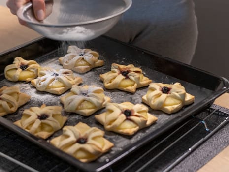 A woman dusts a pineapple wedge and cherry wrapped in a puff pastry with powdered sugar