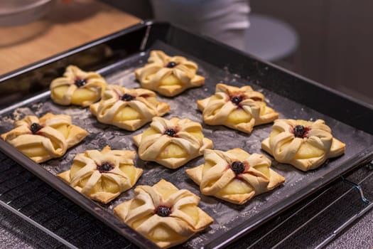 A woman places baking tray with with puff pastry with pineapple wedges wrapped and cherry on top from the oven to the kitchen counter top