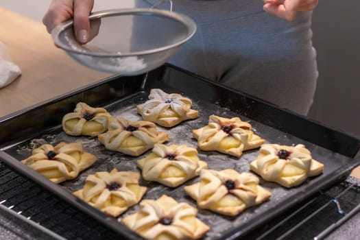 A woman dusts a pineapple wedge and cherry wrapped in a puff pastry with powdered sugar