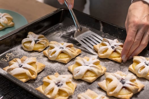 A woman pick the fruit puff pastries with spatula from baking tray and places them on ceramic plate