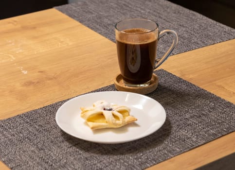 Freshly baked fruit puff pastry on the ceramic plate next to hot cup of coffee