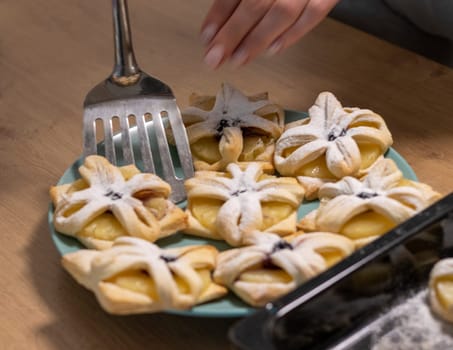A woman pick the fruit puff pastries with spatula from baking tray and places them on ceramic plate