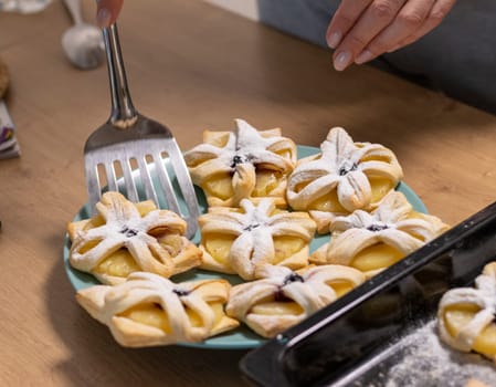 A woman pick the fruit puff pastries with spatula from baking tray and places them on ceramic plate