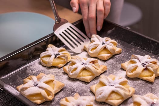 A woman pick the fruit puff pastries with spatula from baking tray and places them on ceramic plate