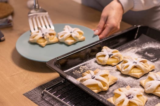 A woman pick the fruit puff pastries with spatula from baking tray and places them on ceramic plate