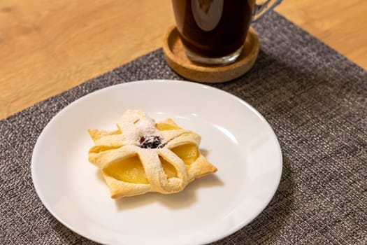 Freshly baked fruit puff pastry on the ceramic plate next to hot cup of coffee