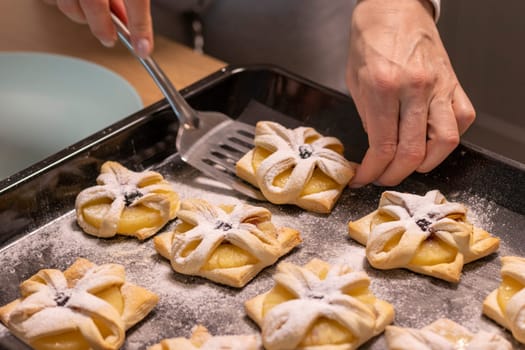 A woman pick the fruit puff pastries with spatula from baking tray and places them on ceramic plate