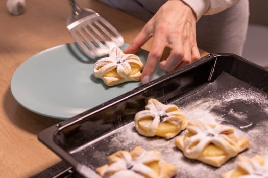 A woman pick the fruit puff pastries with spatula from baking tray and places them on ceramic plate