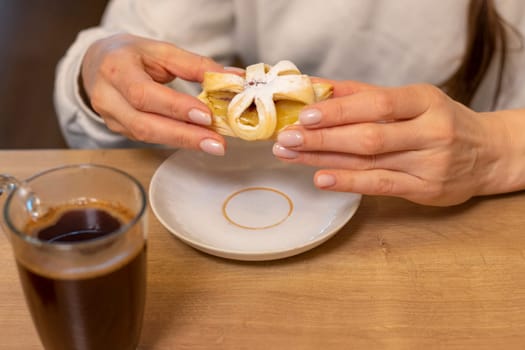 A woman picks freshly baked fruit puff pastry on the ceramic plate next to hot cup of coffee