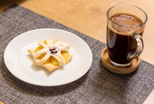 Freshly baked fruit puff pastry on the ceramic plate next to hot cup of coffee