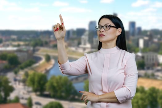 Young asian businesswoman is interacting with invisible virtual screen. Pointing at copy space. Blurred urban scape background.