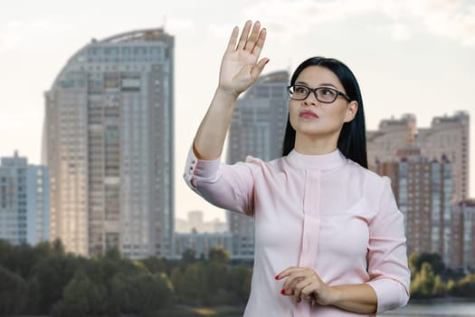 Young asian woman is touching an invisible virtual with her hand. Urban cityscape background.
