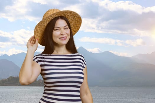 Portrait of a young asian woman wearing straw hat. Mountain and sea background.