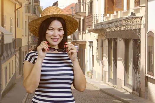Asian female tourist is wearing straw hat. European italian street background.