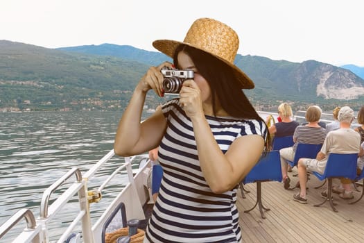 Young woman taking a photo from a yacht deck. Vintage photocamera. Sea water and mountains landscape.